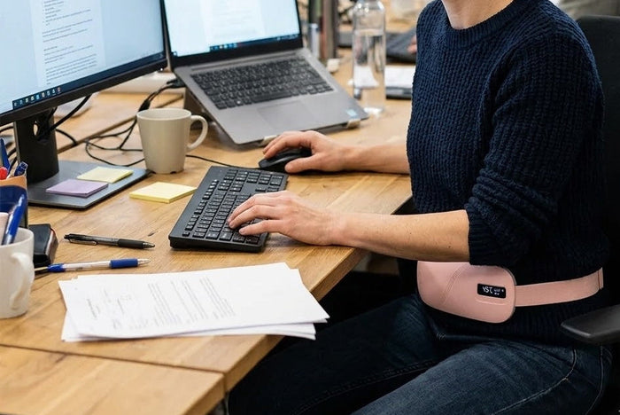 Person using a heated massage pad sitting relaxed and focused at a desk in an office setting